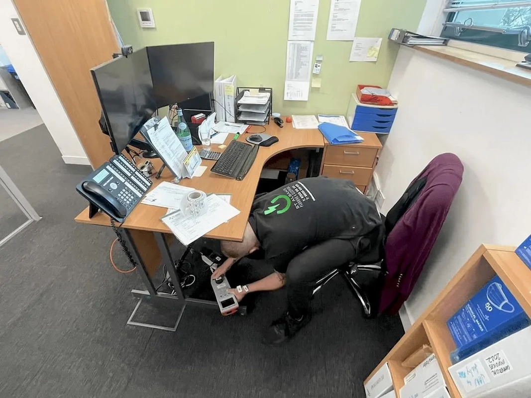 PAT Testing Radlett Engineer PAT Testing electrical equipment, leaning down while sitting in a desk chair holding a pat tester machine